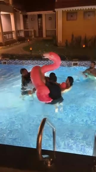 Friends wrestling an inflatable flamingo in a pool at night